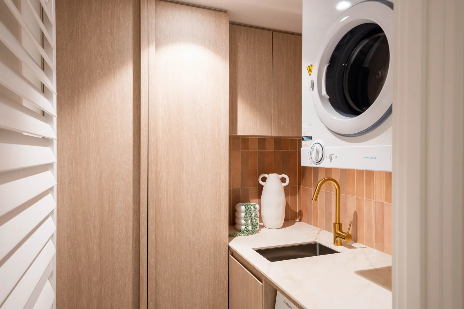 Laundry with fluted timber cabinetry and stacked machines